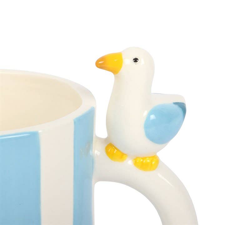 Close-up of ceramic seagull perched on striped mug handle