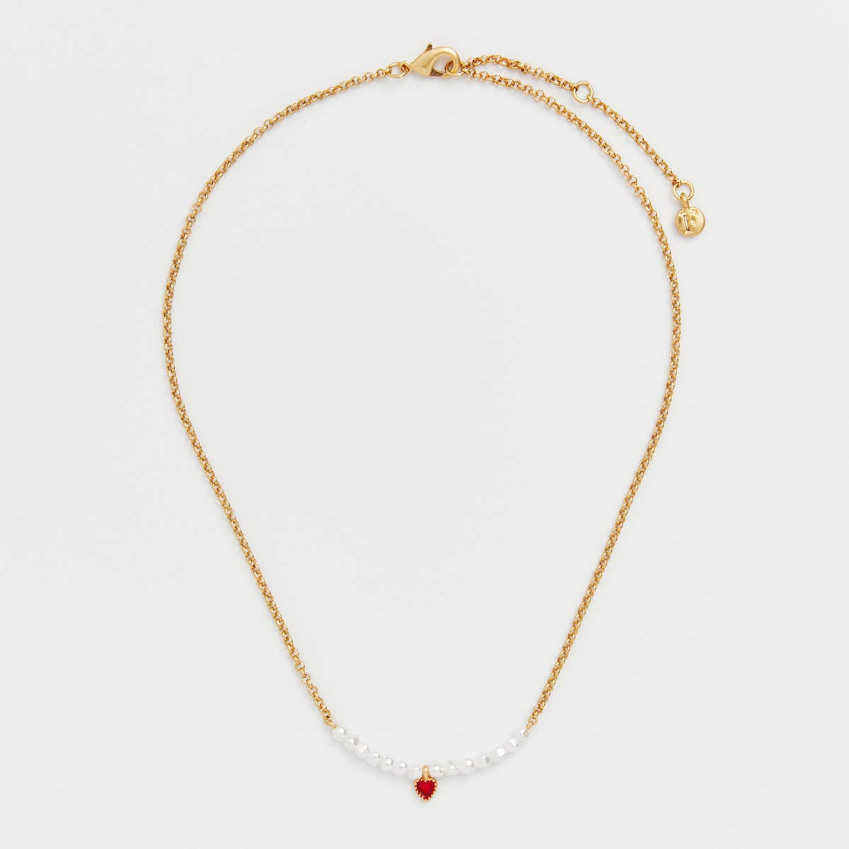 Flat lay of the gold pearl necklace showing the red heart charm at the centre front