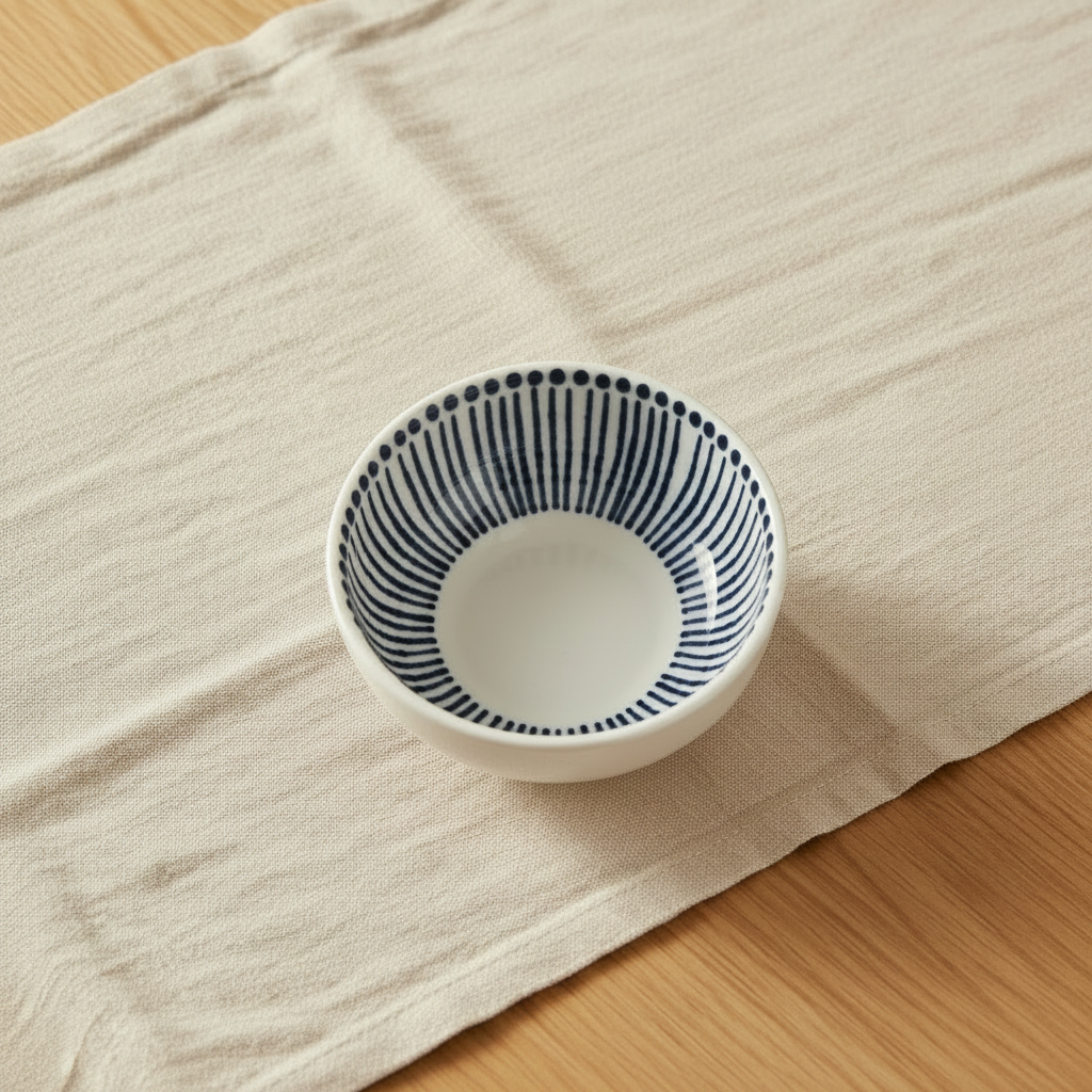 White round ceramic dipping bowl with blue painted line pattern inside, spare copy for lifestyle.