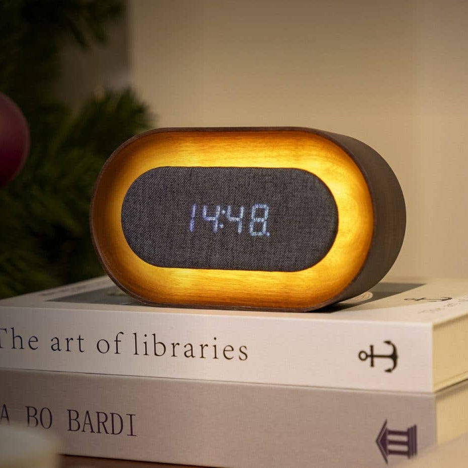 Lumos oval walnut clock glowing warmly on a stack of books