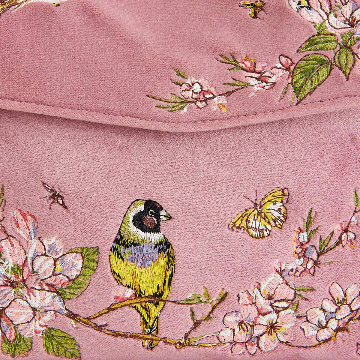 Close-up of embroidered blue tit, blossom and butterfly on pink velvet