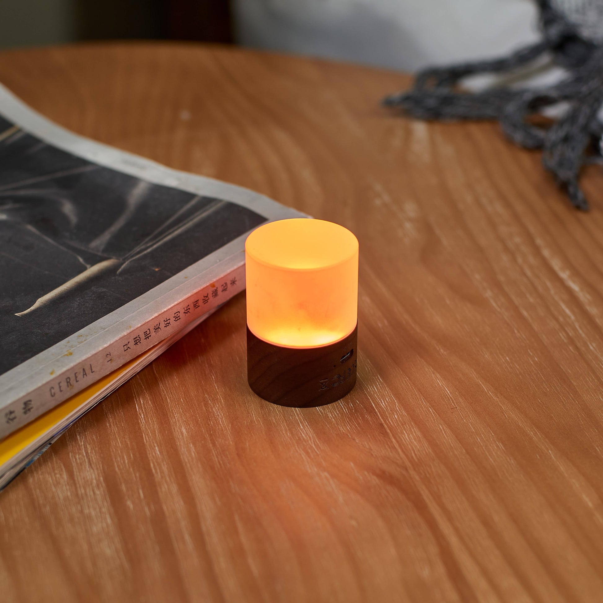 Lemelia mini light glowing amber on a wooden desk beside a magazine