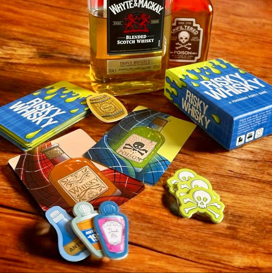 Risky Whisky cards, skull tokens and antidotes on a wooden bar table beside whisky