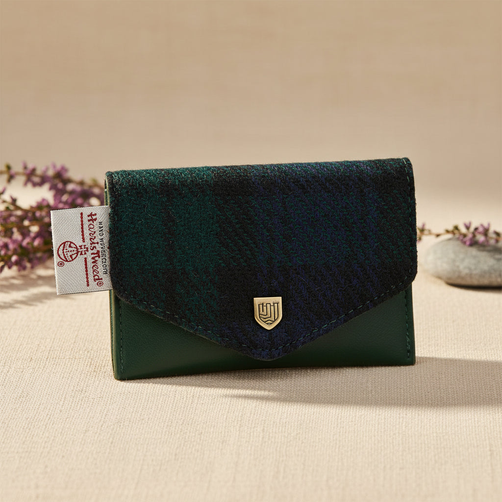 A small envelope-style wallet from The Woolhouse, featuring a dark green leather front and a dark green and black plaid tweed flap. A small gold shield logo is centered on the flap, and a white brand tag is visible on the left side.