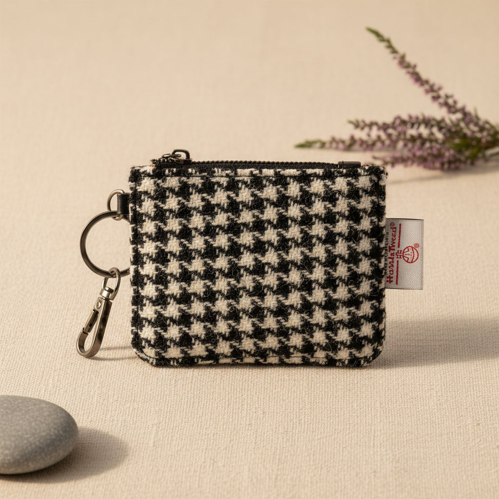A small zippered pouch with a black and off-white houndstooth pattern, featuring a silver-tone key ring and clasp on the left and a white fabric brand tag on the right.