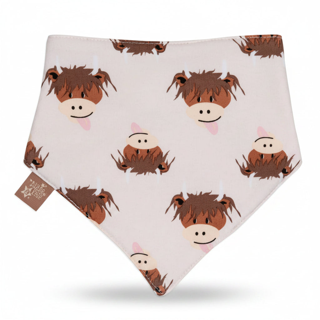 A white baby bandana bib featuring a playful pattern of cartoon brown highland cow with pink tongues, displayed against a split orange and beige background.