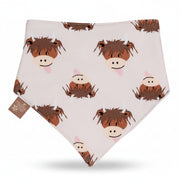 A white baby bandana bib featuring a playful pattern of cartoon brown highland cow with pink tongues, displayed against a split orange and beige background.
