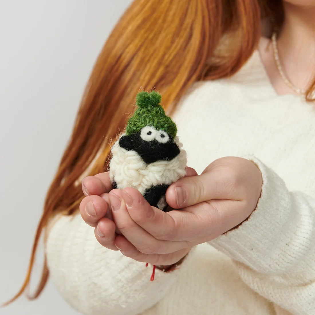 Person holding a small knitted sheep keyring with a green hat.