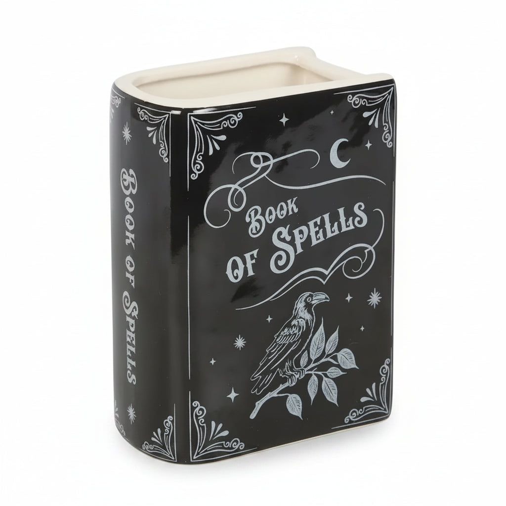 Angled front view of ceramic spellbook vase. Black and white ceramic flower vase shaped like a spellbook with ‘Book of Spells’ text and raven illustration on front.