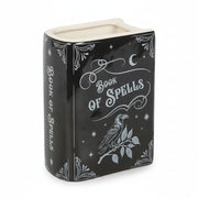 Angled front view of ceramic spellbook vase. Black and white ceramic flower vase shaped like a spellbook with ‘Book of Spells’ text and raven illustration on front.