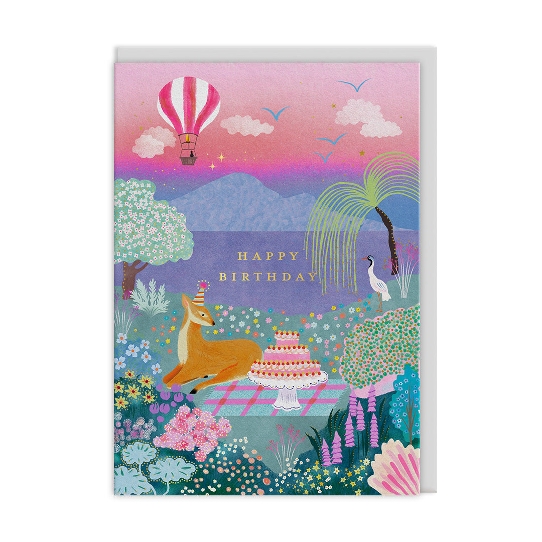 Pastel birthday card with deer in party hat beside tiered cake by a lake