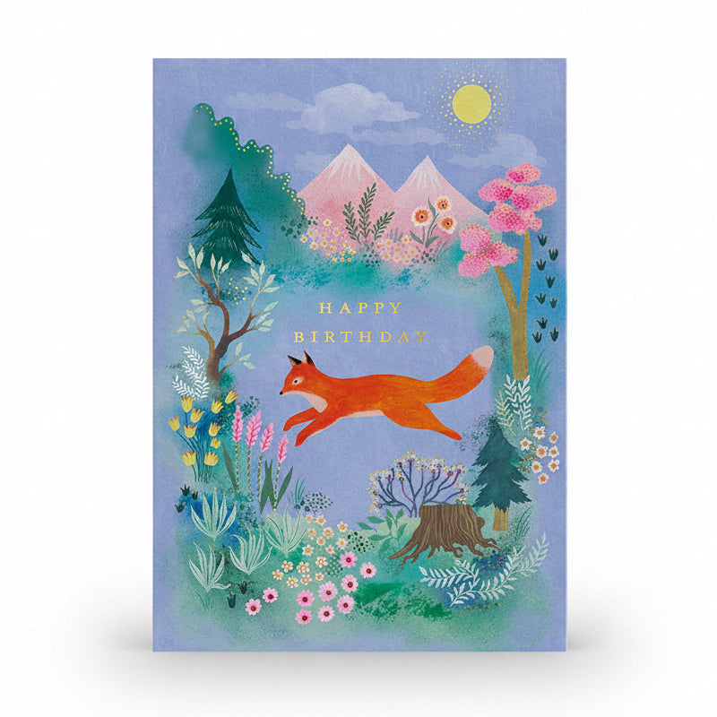 Blue birthday card with an orange fox leaping across a mountain meadow