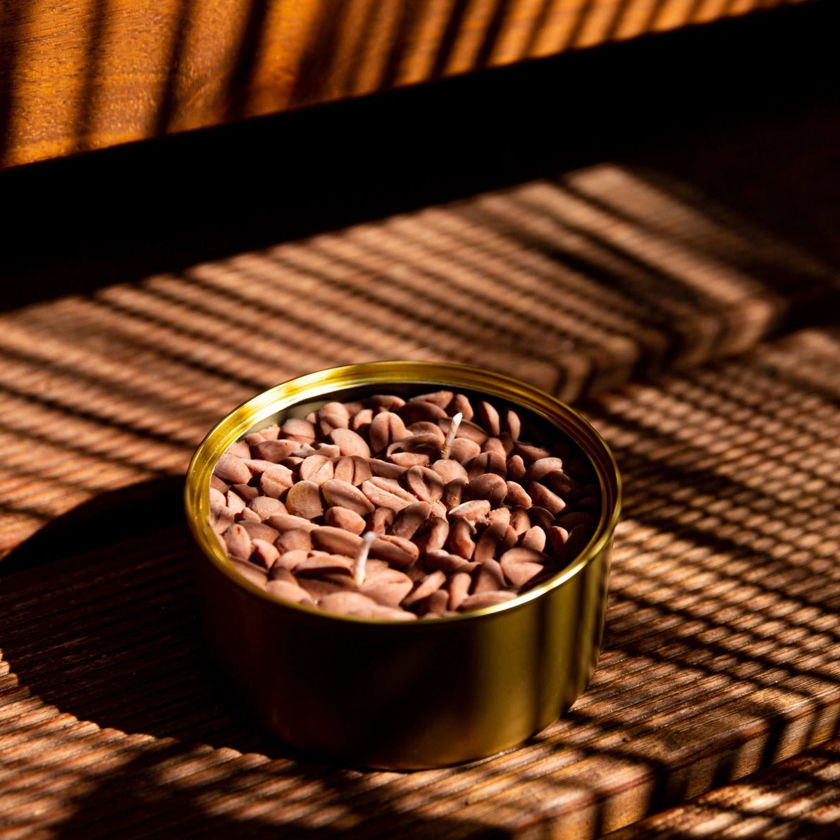 Coffee bean candle in golden tin placed in dappled sunlight on a rustic wooden surface, highlighting the rich texture and realistic wax beans.