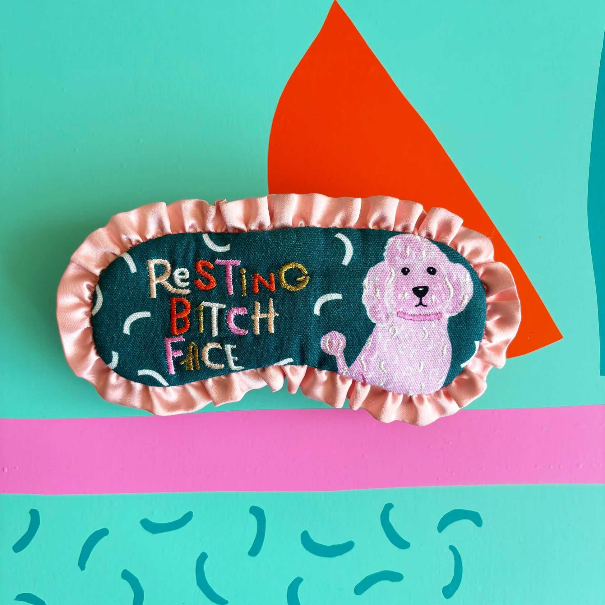 Resting Bitch Face eyemask on teal and pink patterned background.