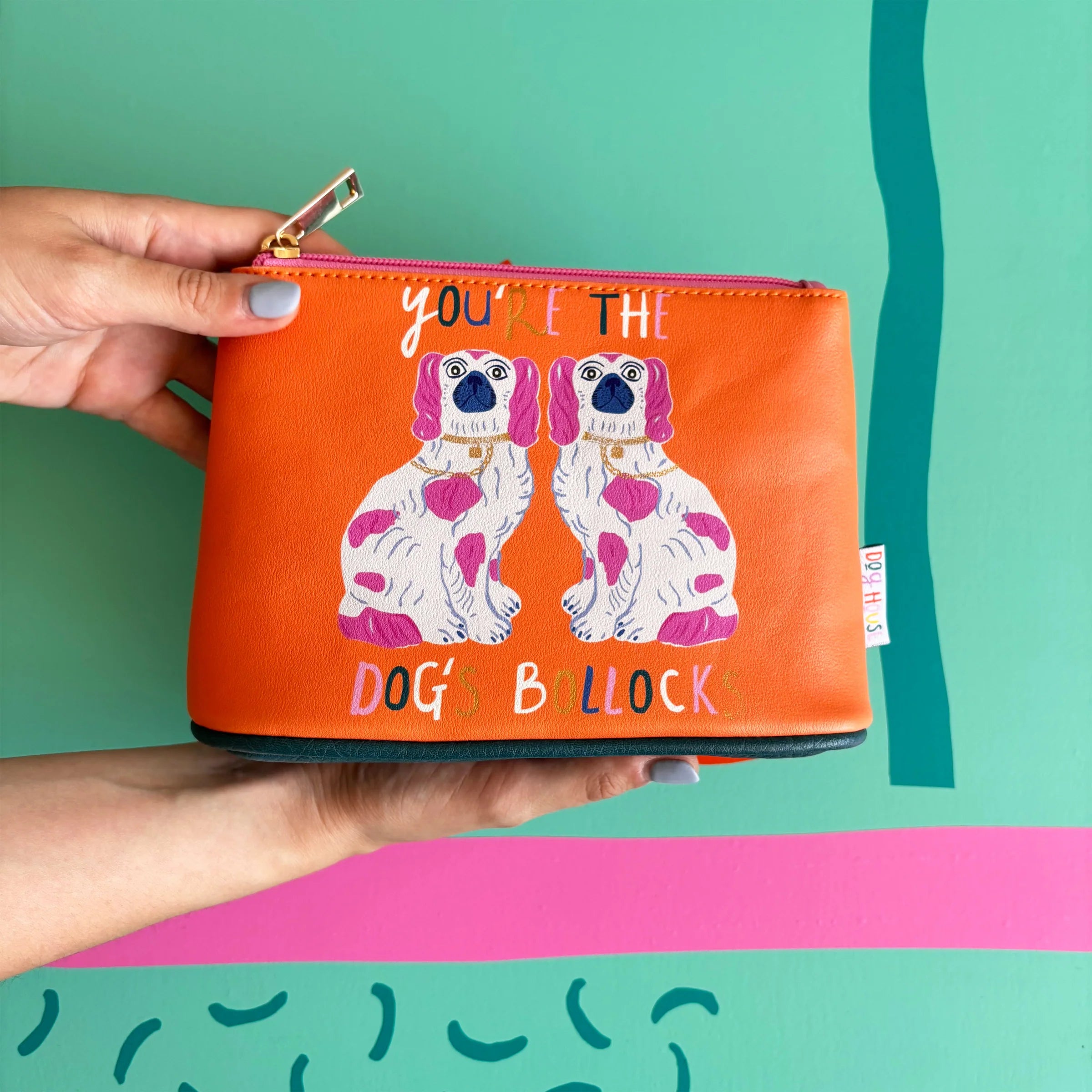 Person holding Dogs Bollocks Makeup Bag with twin dog print and pink zip.