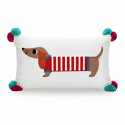 White oblong embroidered cushion with sausage dog design and red and blue pom poms on corners.