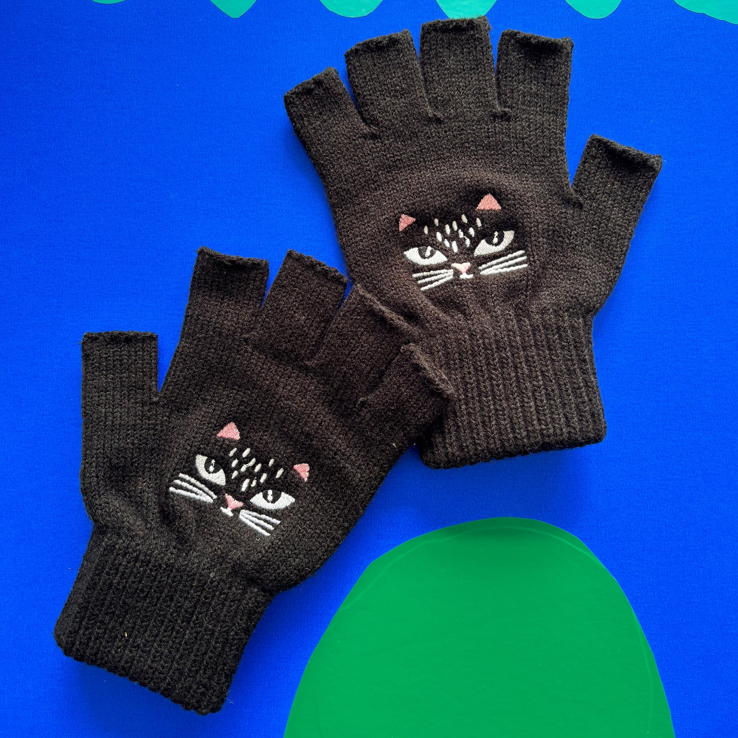 Pair of black cat design gloves displayed on colourful backdrop.