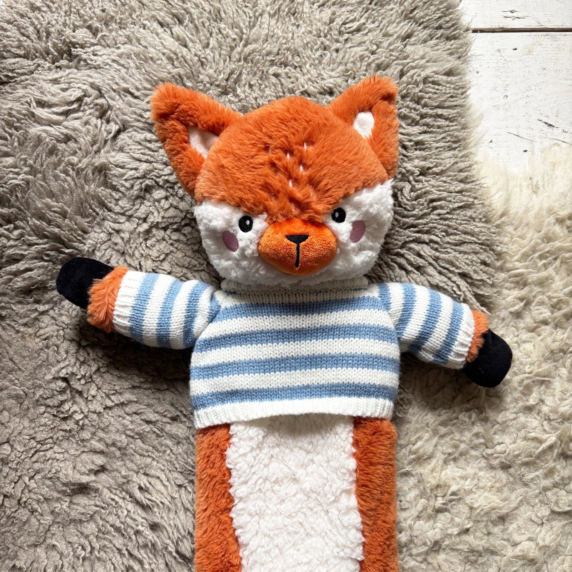 Close-up of fox hot water bottle showing embroidered face and blue striped jumper.
