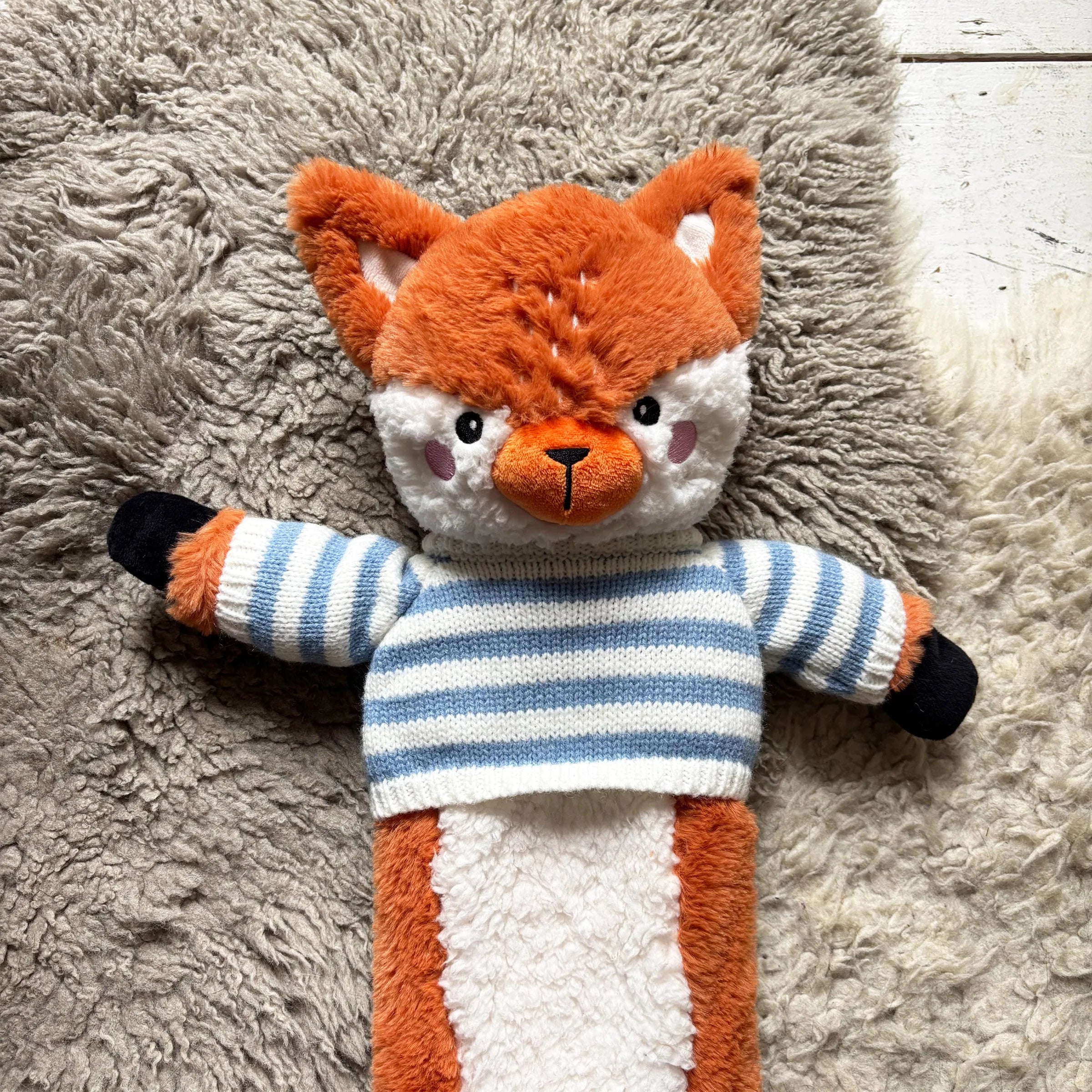 Close-up of fox hot water bottle showing embroidered face and blue striped jumper.