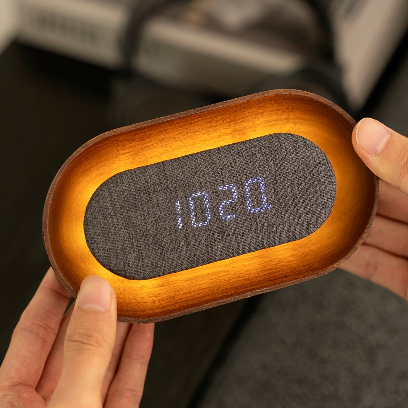 Hand holding glowing Lumos oval walnut alarm clock