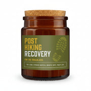 An amber glass jar with a cork lid and a green label reading 'POST HIKING RECOVERY' in yellow and white text, set against a textured gray background.