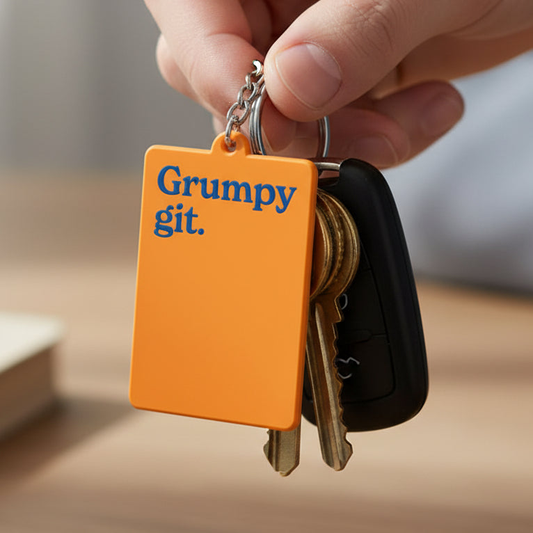 Bright orange keyring that says grumpy git in blue writing across the front. 