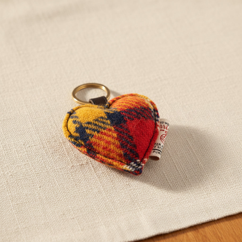 A heart-shaped felt keychain charm in a red, yellow, and navy tartan plaid pattern, attached to a dark brown leather loop and a metal key ring, shown on a white background.