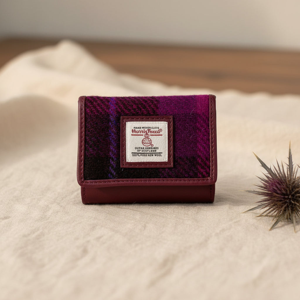 A small Harry Tweed trifold wallet featuring a textured purple and magenta plaid pattern on the front flap, with a white brand label in the center and a dark burgundy leather base.