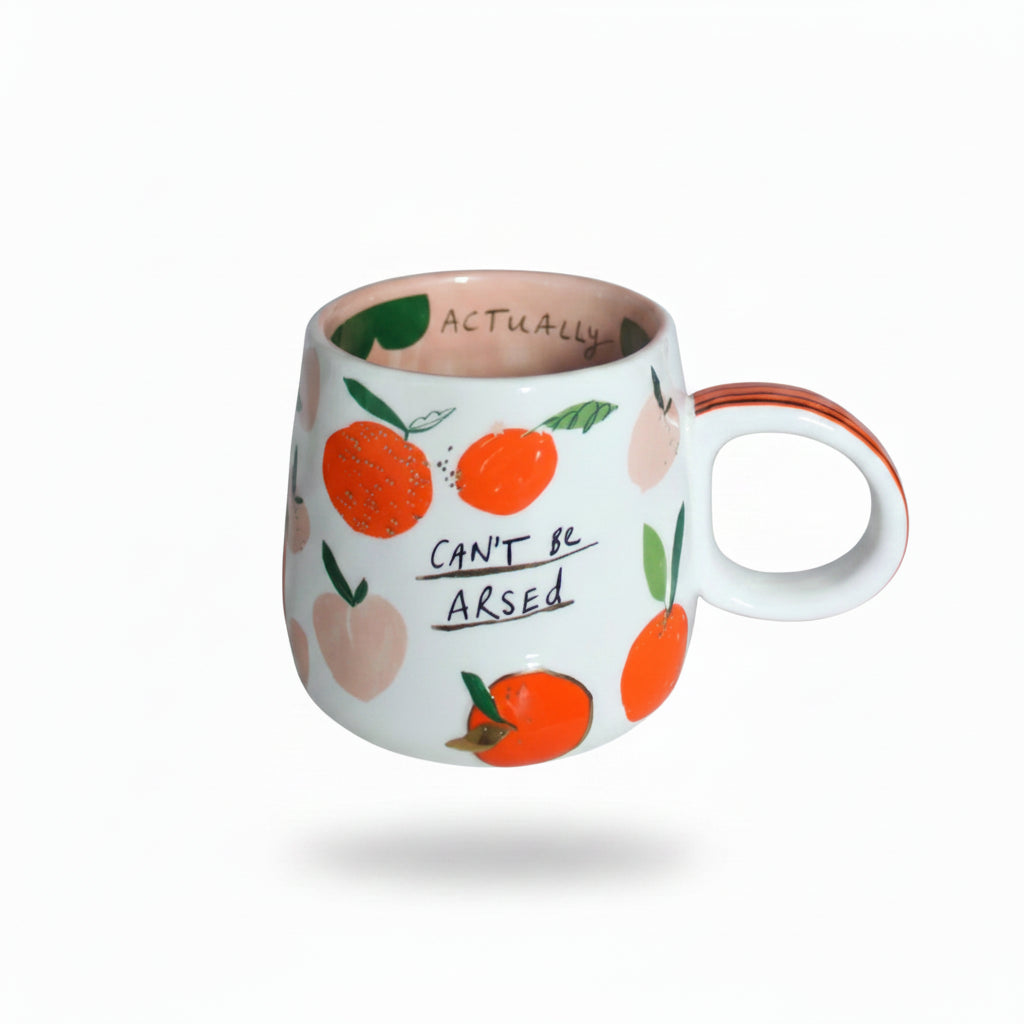 Funny handmade-style mug with orange and peach design, sitting on a shelf with the hidden message “Actually” visible inside the rim.