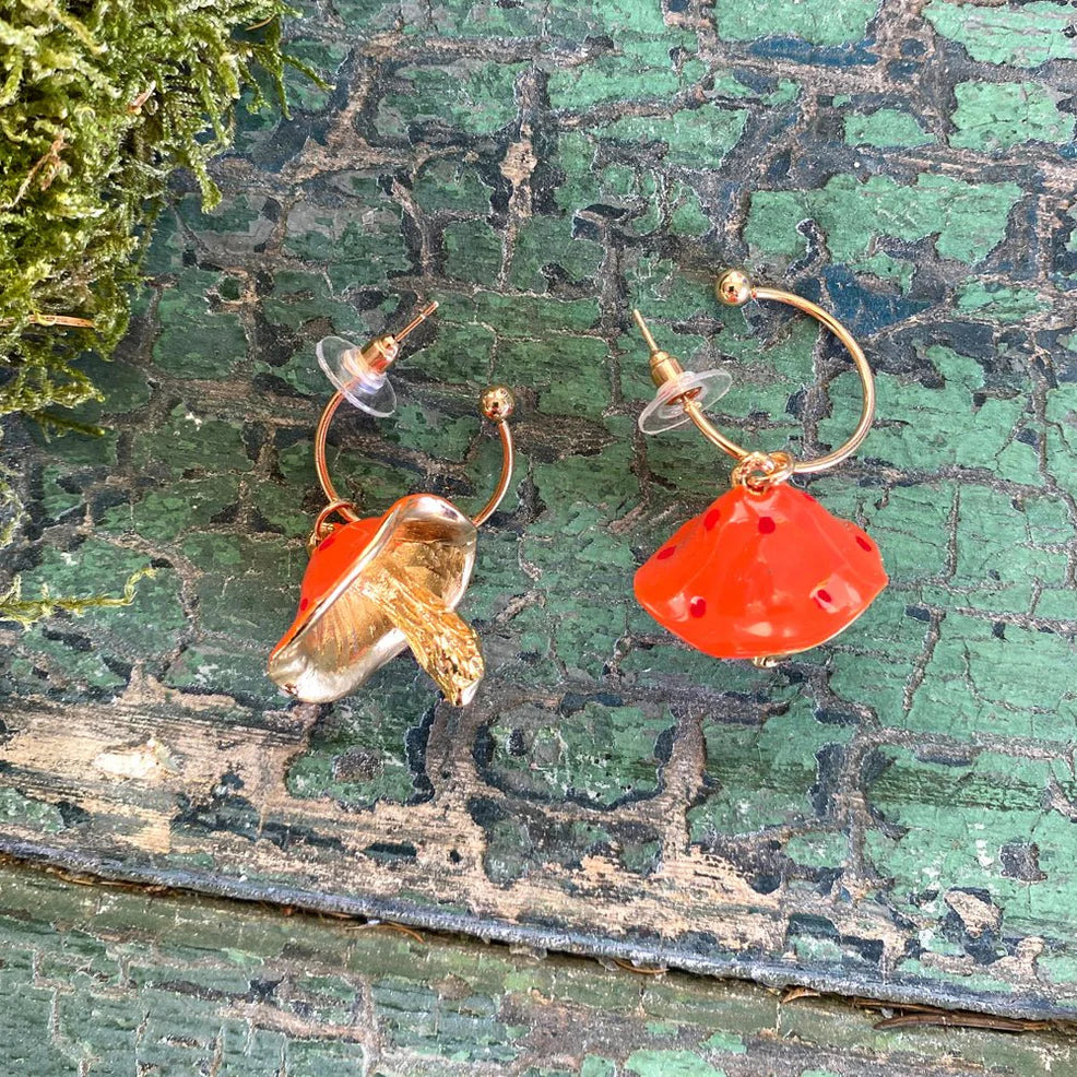 Flat lay of Forage Red Earrings showcasing front and back details—red glazed mushroom cap with gold stalk and interior gold gill detailing, on rustic green backdrop.