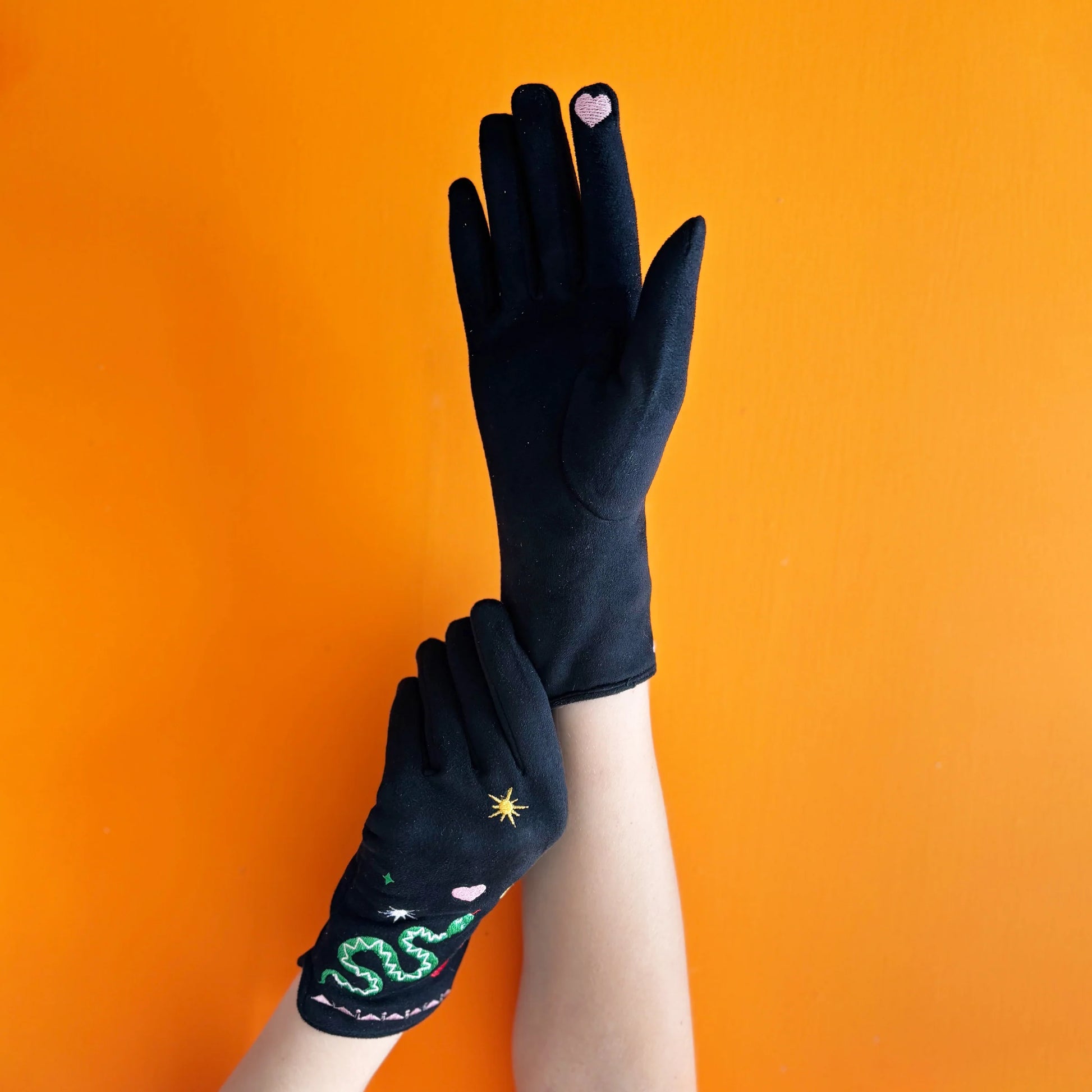Model showing black suedette snake gloves with embroidered designs and pink heart on fingertip.