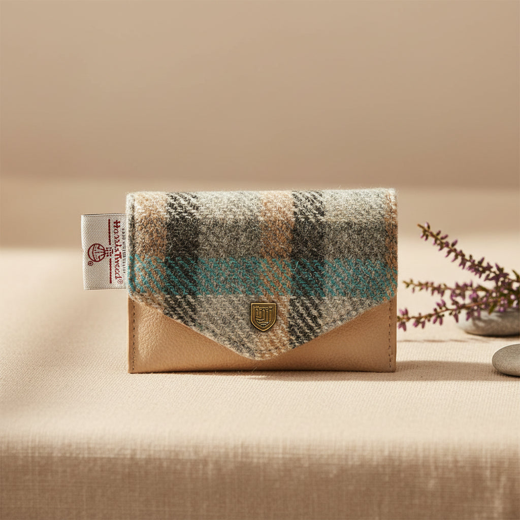 A small wallet or card case from Harris Tweed, featuring a beige pebbled leather base and a flap made of a plaid wool-like fabric in beige, gray, black, and turquoise blue. A gold shield logo is on the front, and a white brand tag is visible on the left.