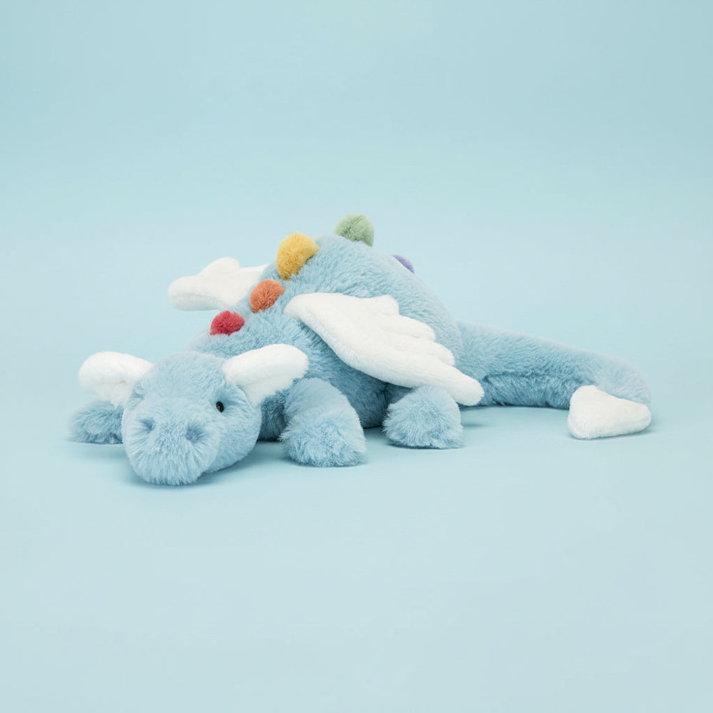 A light blue plush dragon toy with white wings, small colorful spikes, and red, yellow, and green accents, photographed on a clean white background.
