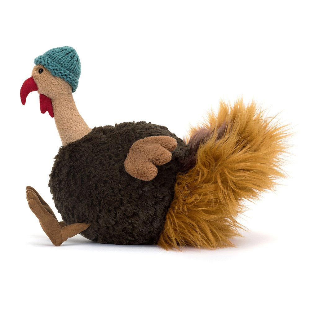 Jellycat Theo Turkey plush sitting with wings out and teal knitted hat.