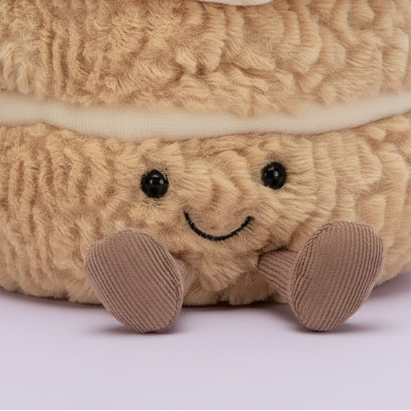 A plush cake-shaped pillow with cream-colored frosting, red velvet cake layers, a single red-and-white striped candle, and a smiling face, photographed on a clean white background.