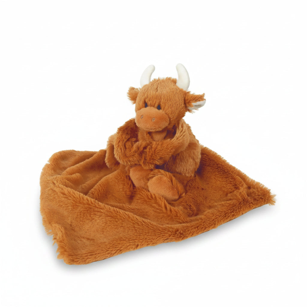 Plush toy Highland cow with a blanket on a light wooden surface