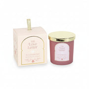 The Love Letter Rose & Vanilla Musk Candle in pink jar with gold lid displayed next to decorative illustrated gift box with gold ribbon handle.