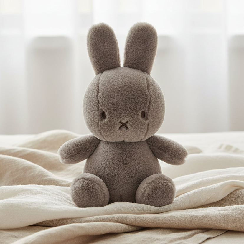 Miffy Cozy taupe plush sitting on cream linen bedding lifestyle