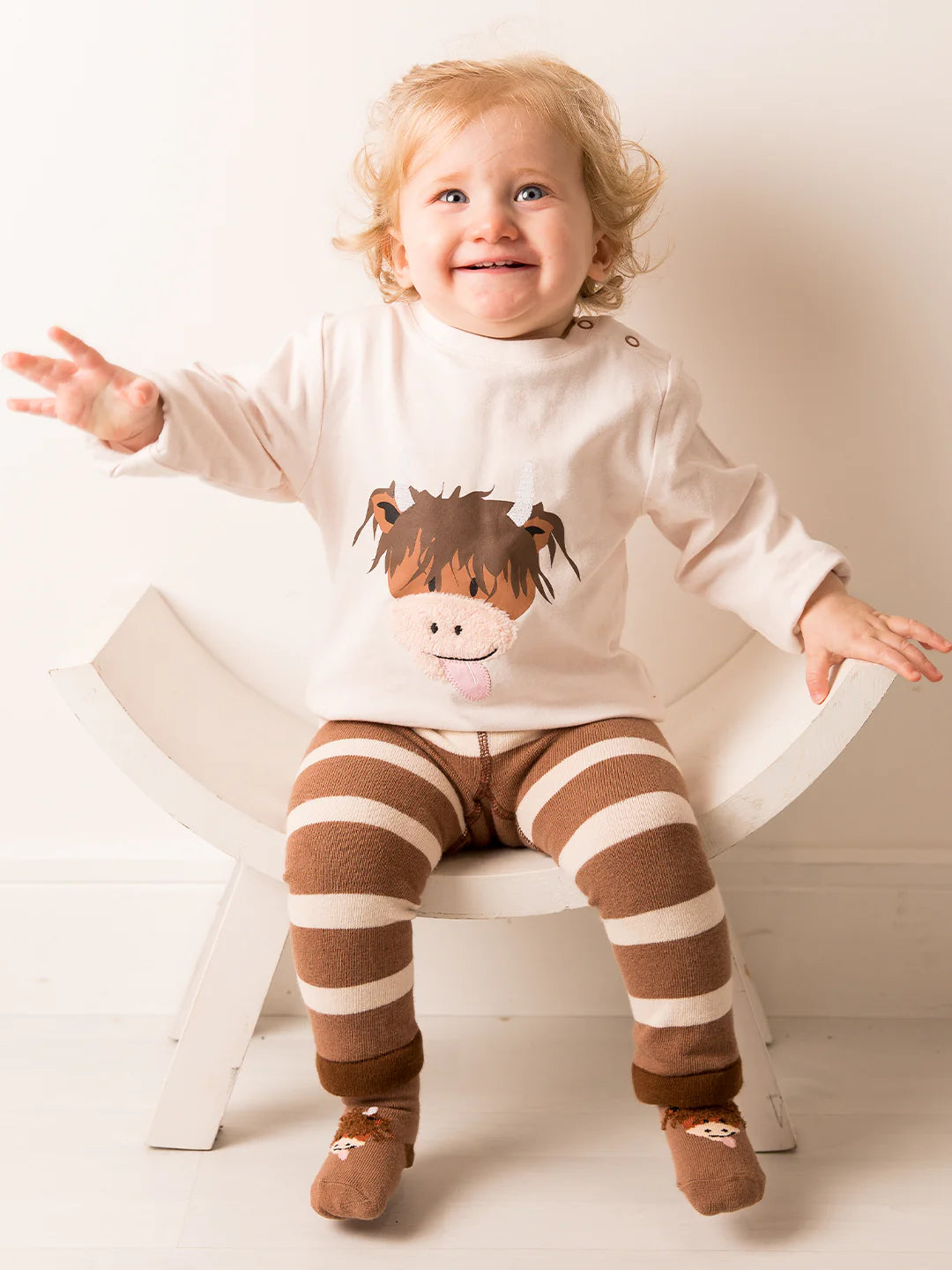 Baby sitting in a full outfit with Neutral Highland Cow Leggings and matching cow-themed top.