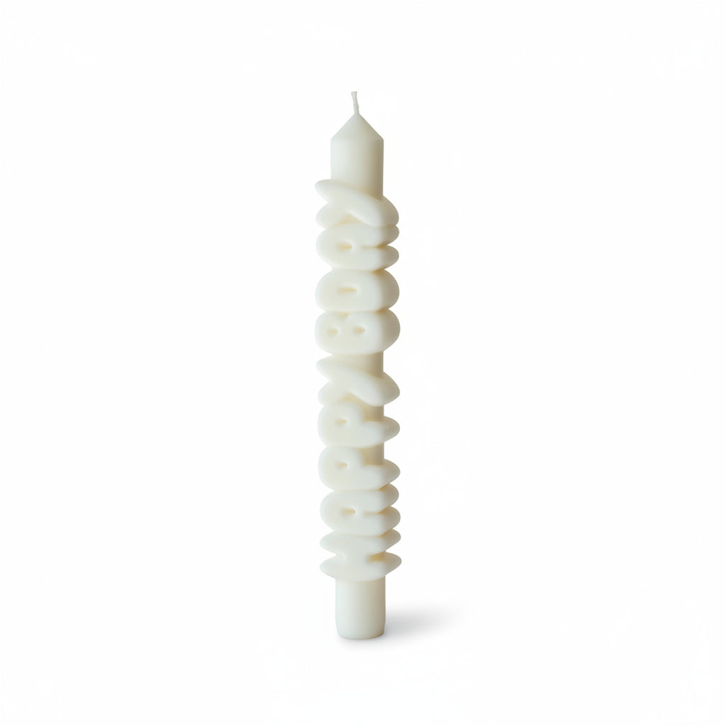 Person holding a white 9-inch handmade taper candle with raised 3D “HAPPY BDAY” lettering, made from soy-paraffin wax blend, against a neutral curtain background.