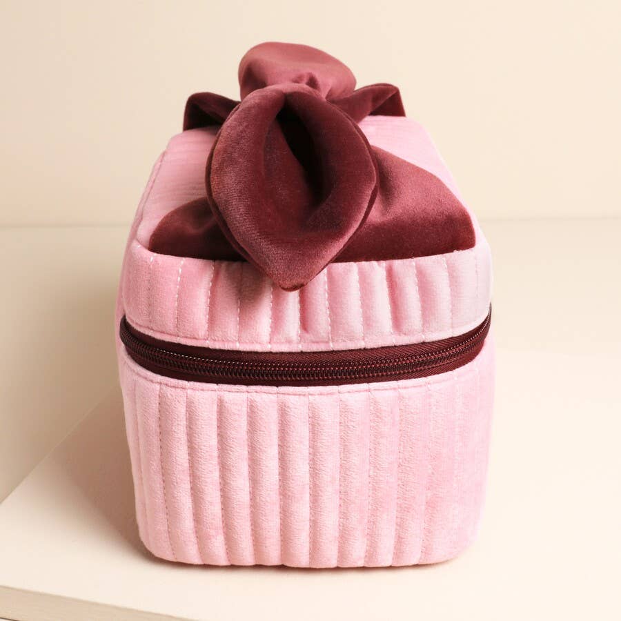 Side view of ribbed pink velvet makeup bag with red bow detail.