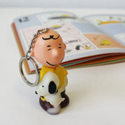 Close-up of Peanuts Charlie Brown & Snoopy Light-Up Keyring next to a Peanuts comic book.