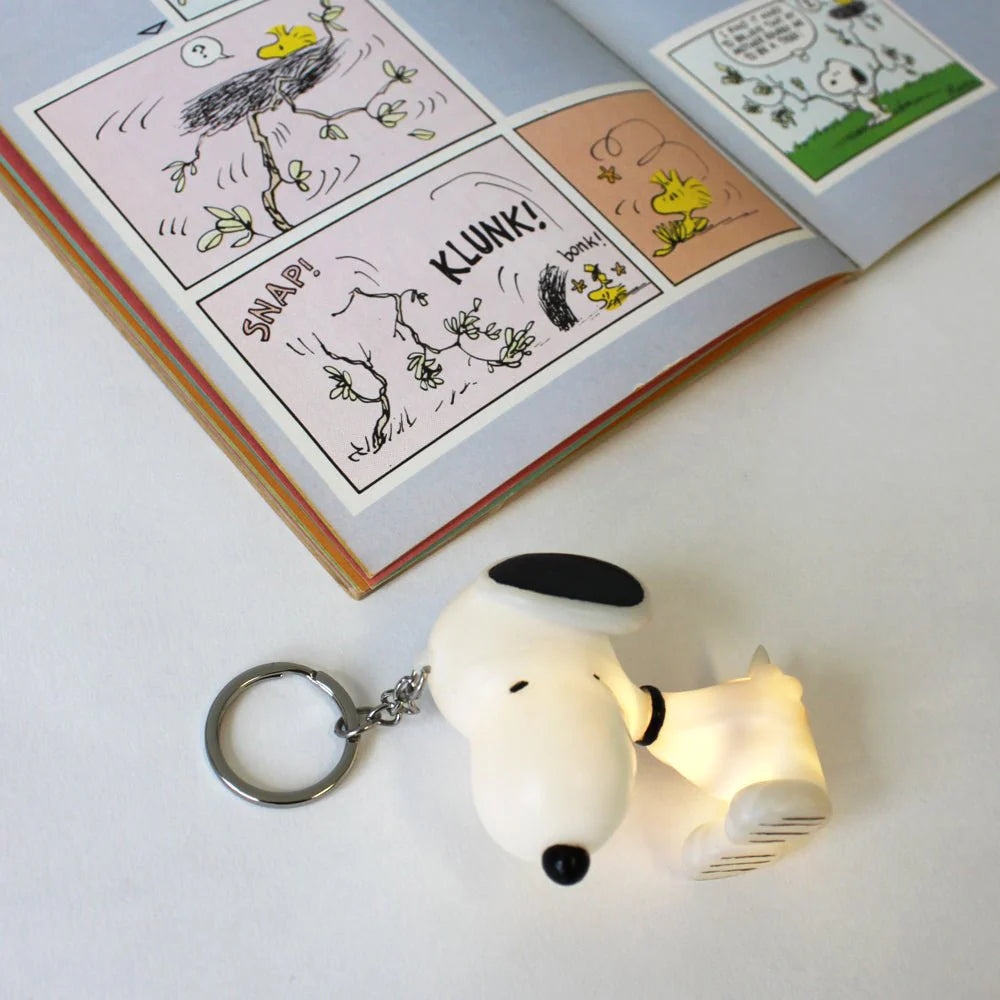 Close-up of the Peanuts Snoopy Light-Up Keyring next to an open comic book.