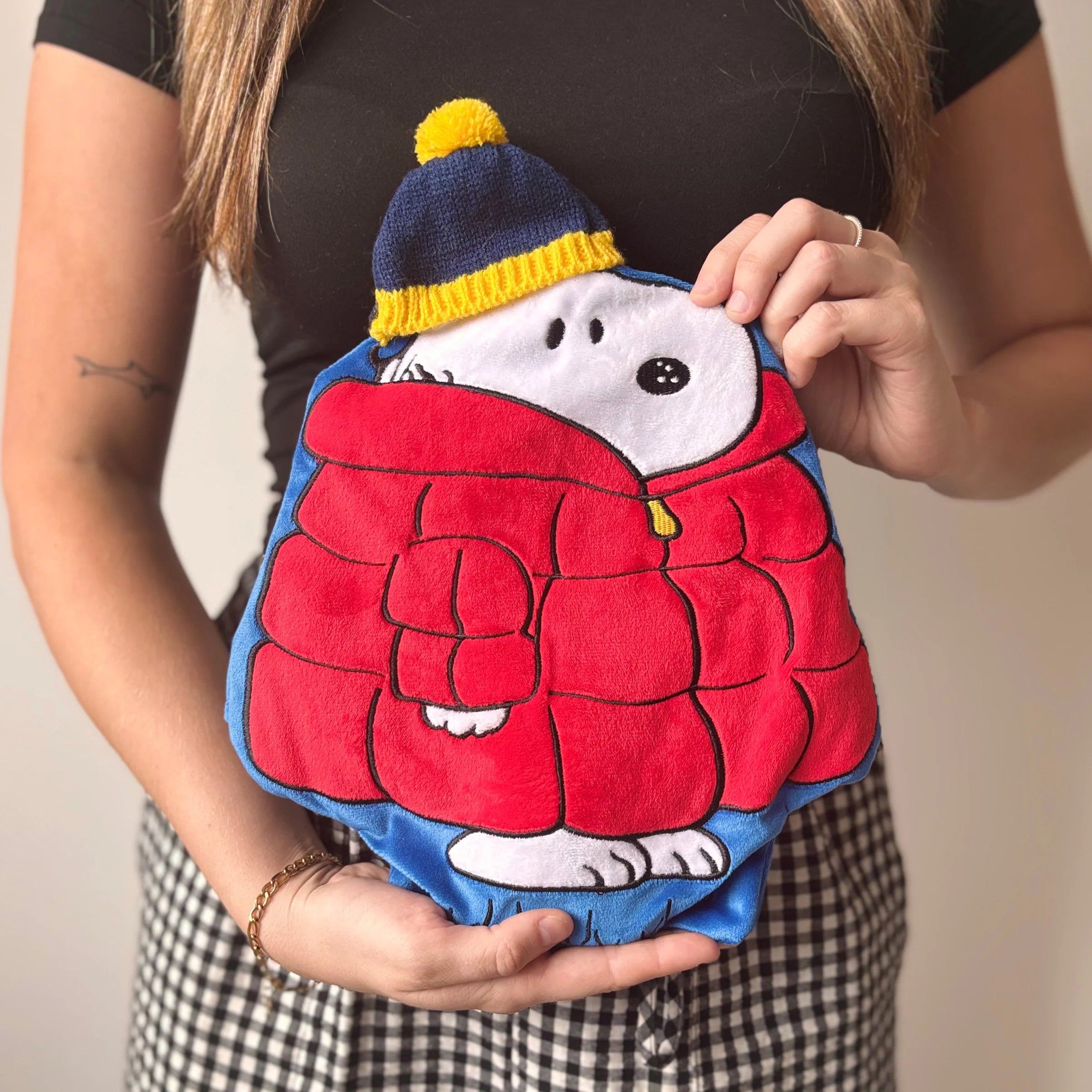 	Woman holding Peanuts Snoopy Puffa Hot Water Bottle with red puffa coat design.