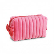 Pink velvet makeup bag with red bow and zip on cream background.