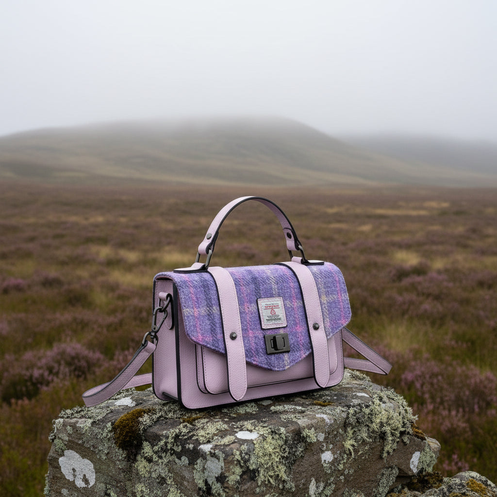A lavender and purple plaid handbag with light purple leather straps and handles, featuring a central brand patch and a black turn-lock closure, set against a plain white background.