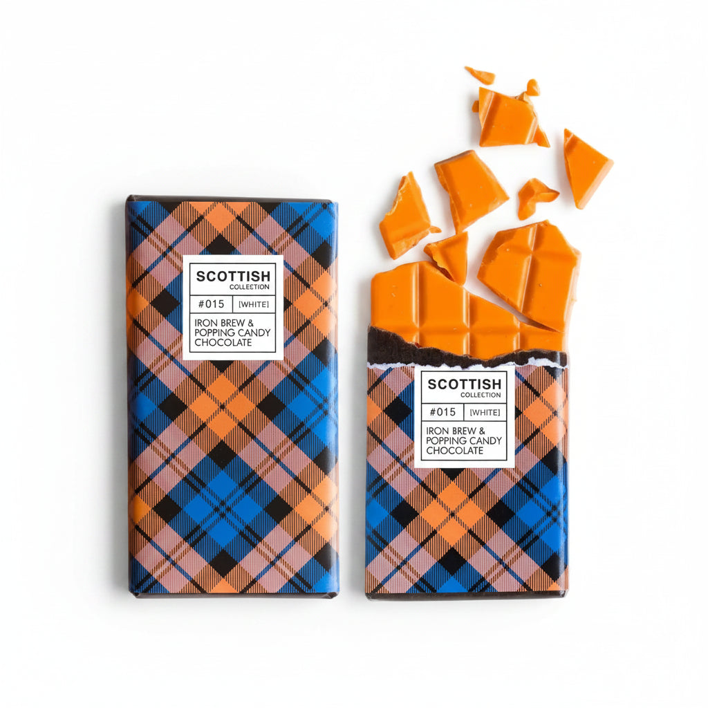 Two bars of Scottish Whiskers #015 Bon Brew & Popping Candy Chocolate are arranged on a white surface, with one bar whole and the other cracked open to show the bright orange filling. A glass of orange beverage is partially visible in the top-left corner.