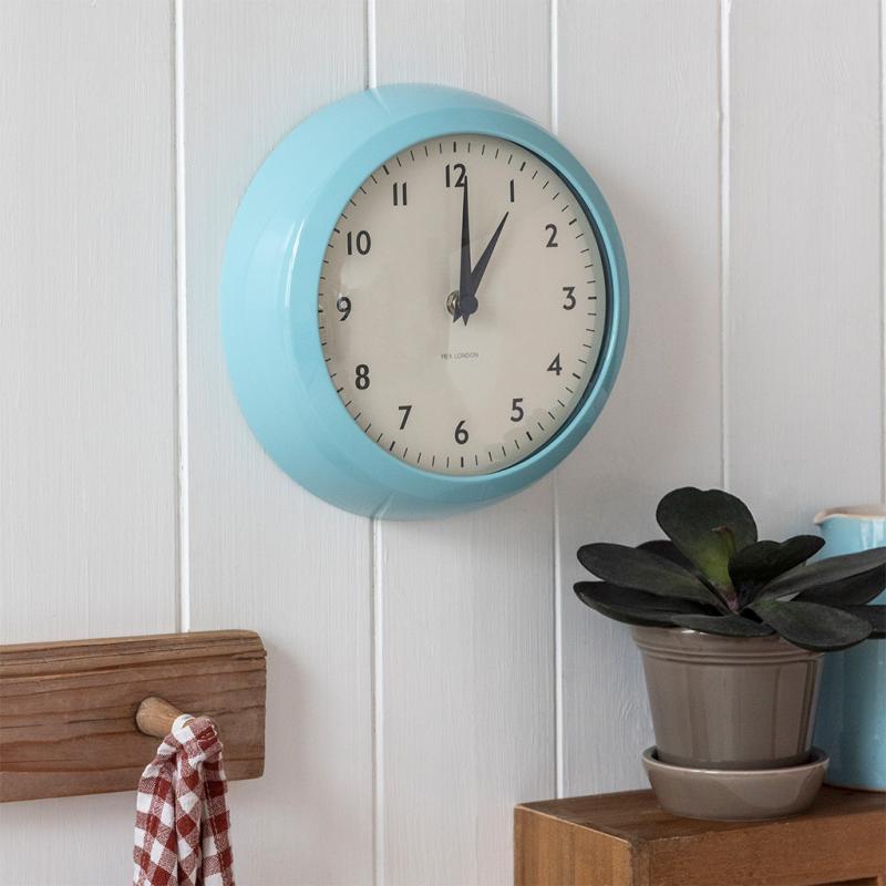 Blue retro wall clock on white wood panelling with shelf and plant