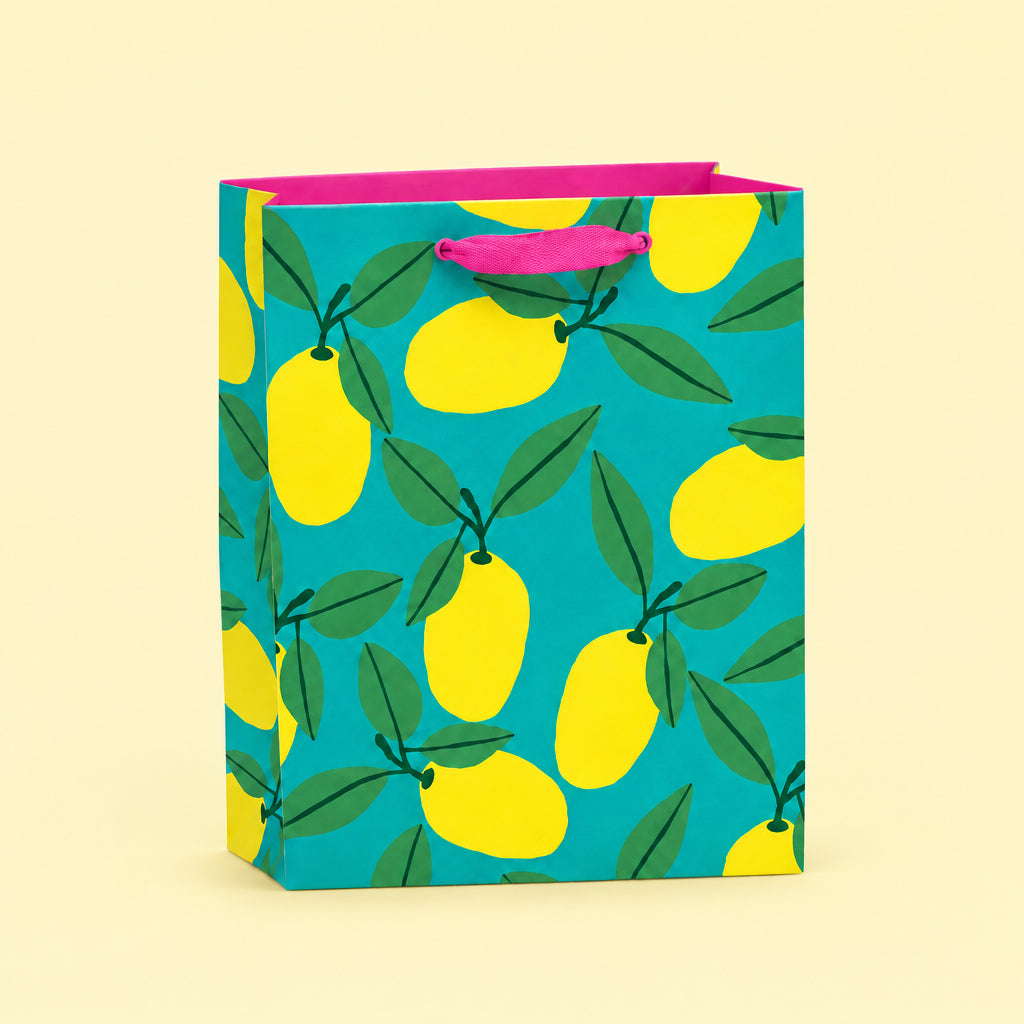 A square gift bag with a bright turquoise background and a repeating yellow lemon and green leaf pattern, finished with hot pink handles and inner lining, shown on a plain white background.