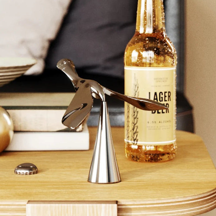Umbra Tipsy bottle opener chrome leaning against beer bottle on books
